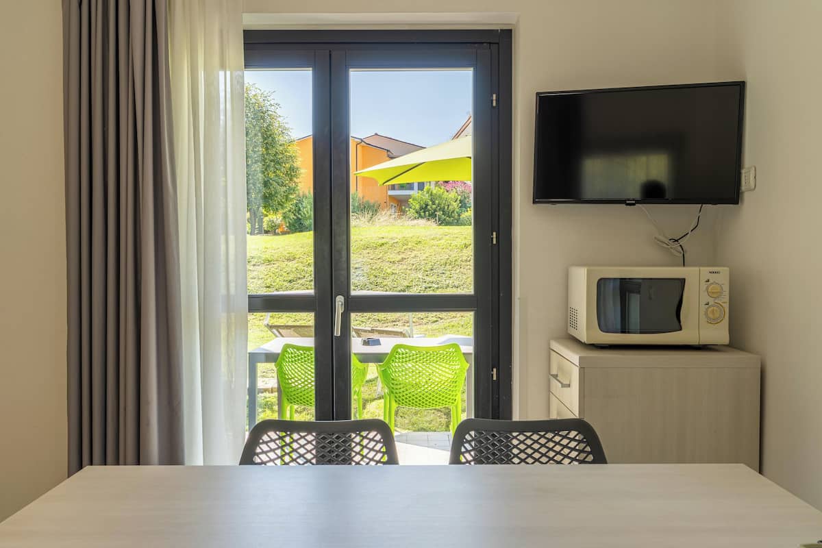 Een kamer met een eettafel, twee stoelen, een aan de muur bevestigde televisie en een magnetron op een kast.