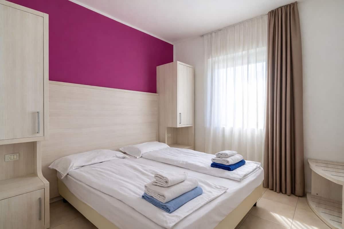 Een hotelkamer met twee bedden, een paarse accentmuur en een raam met gordijnen.