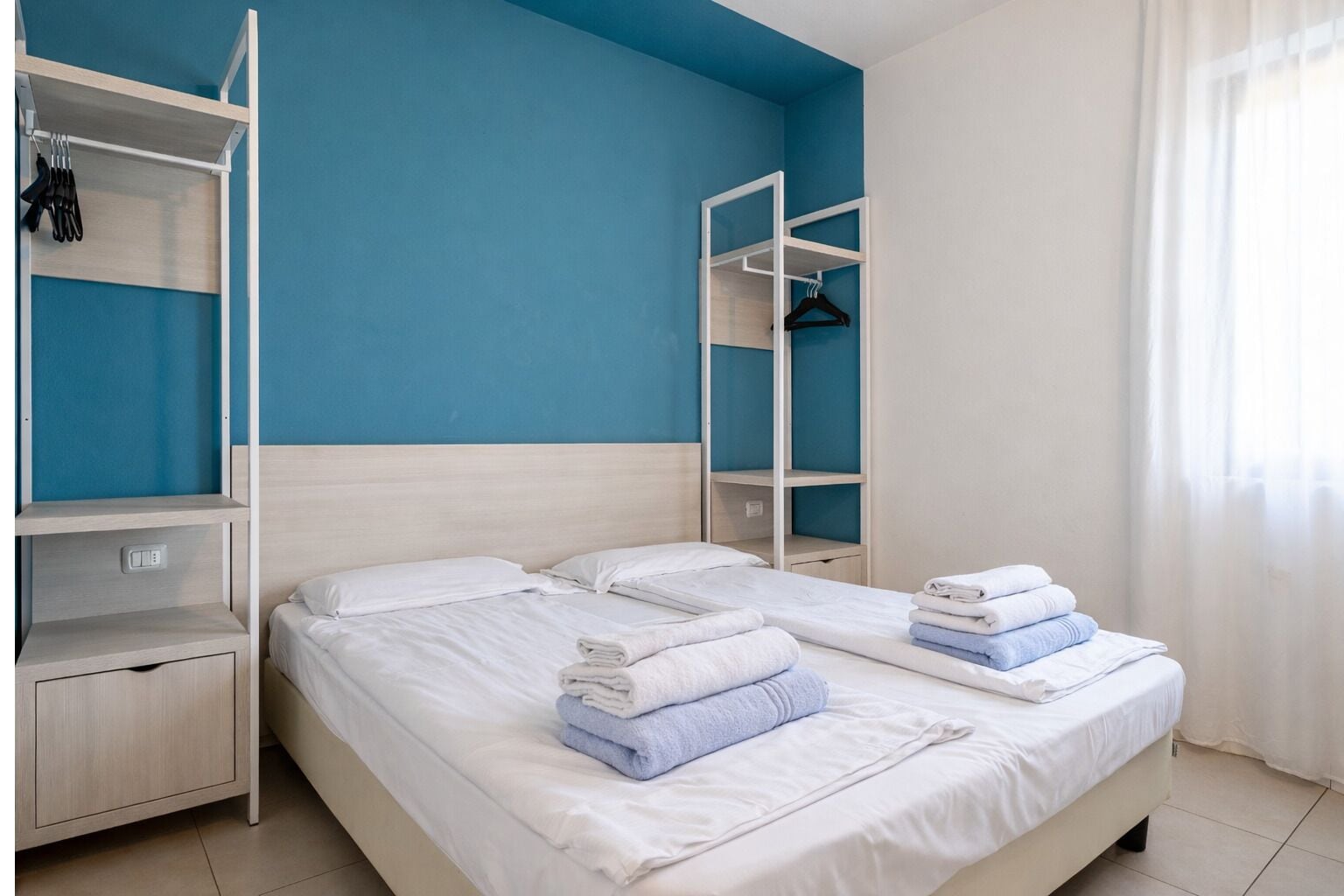 Habitación de hotel con dos camas, un armario y una repisa con toallas.