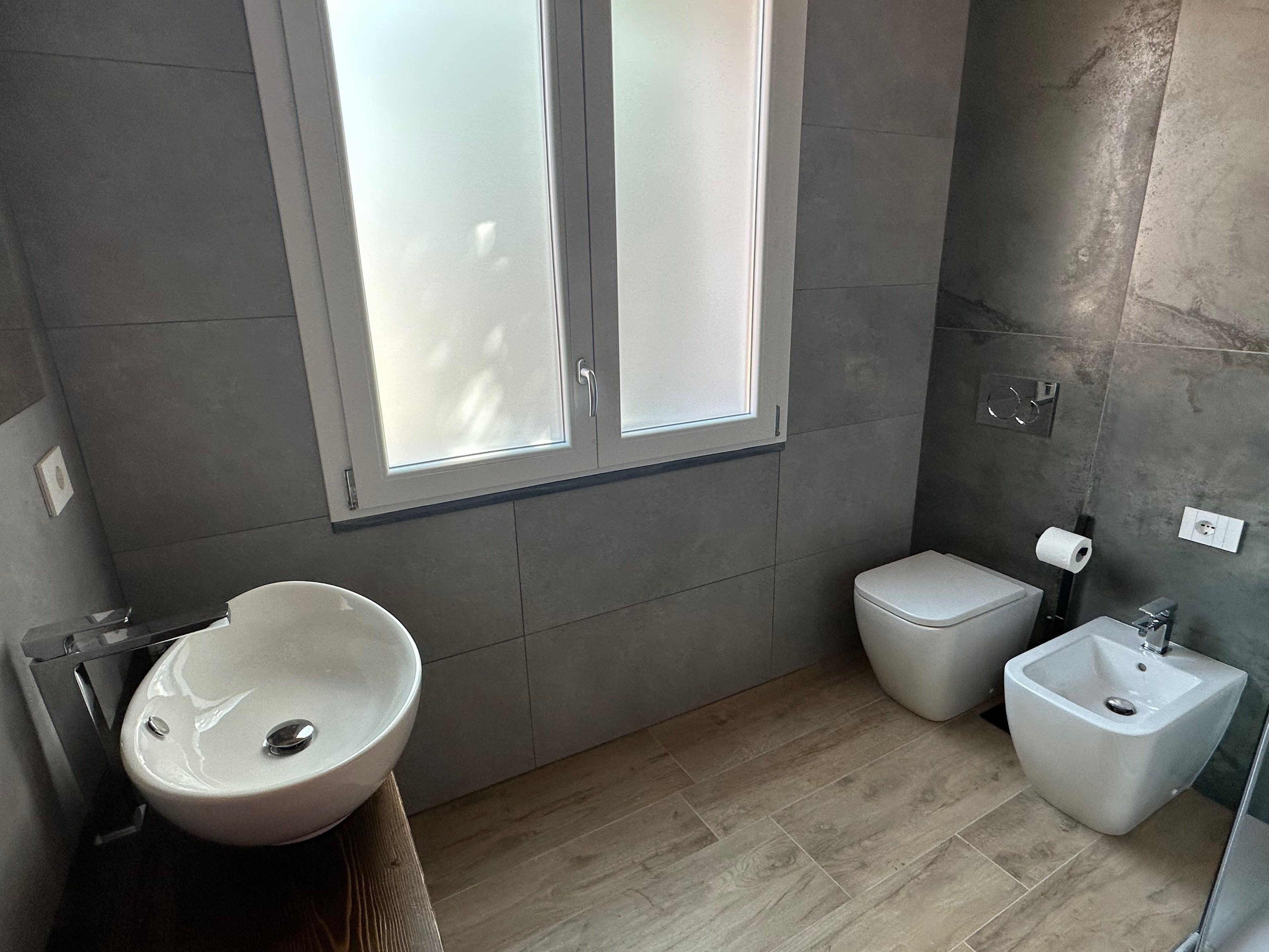 A modern bathroom with a large window, a sink, a toilet, and a bidet.