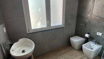 A modern bathroom with a large window, a sink, a toilet, and a bidet.