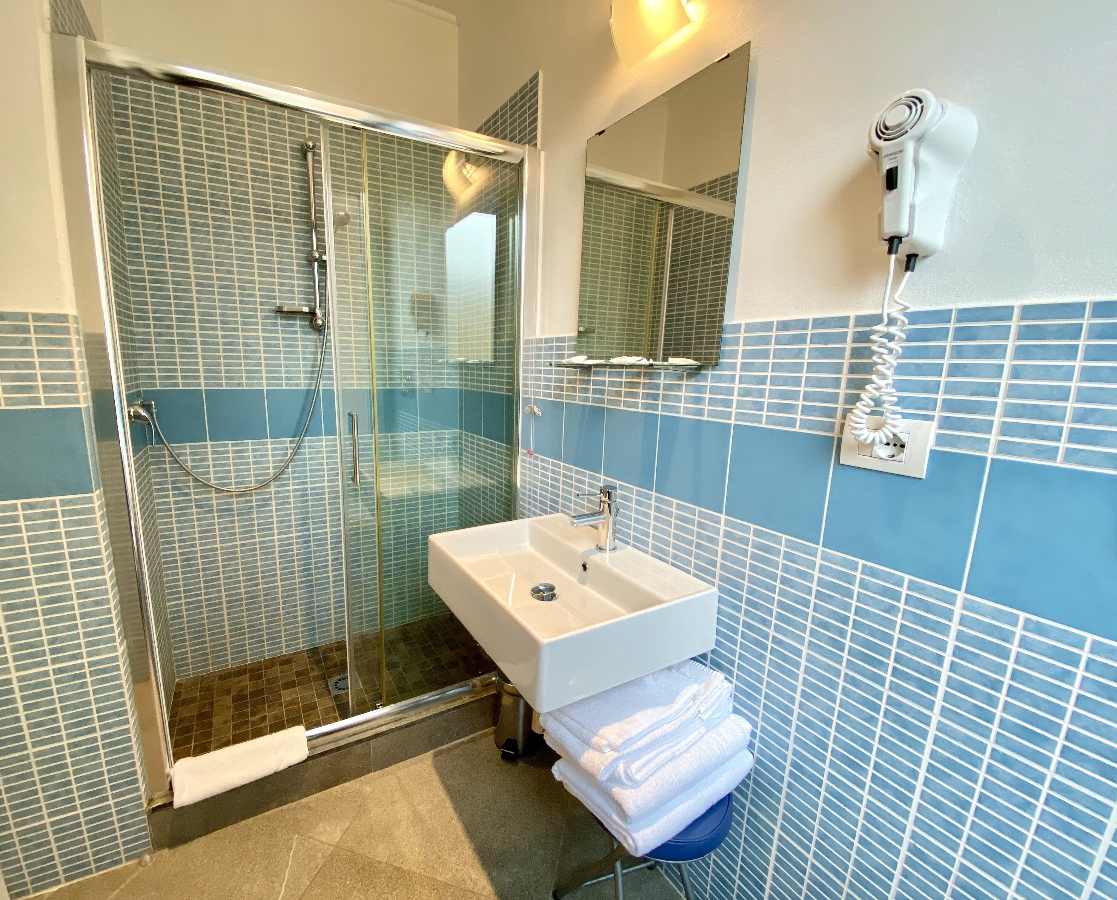 A bathroom with a glass-enclosed shower, a white sink, and a towel rack with towels.