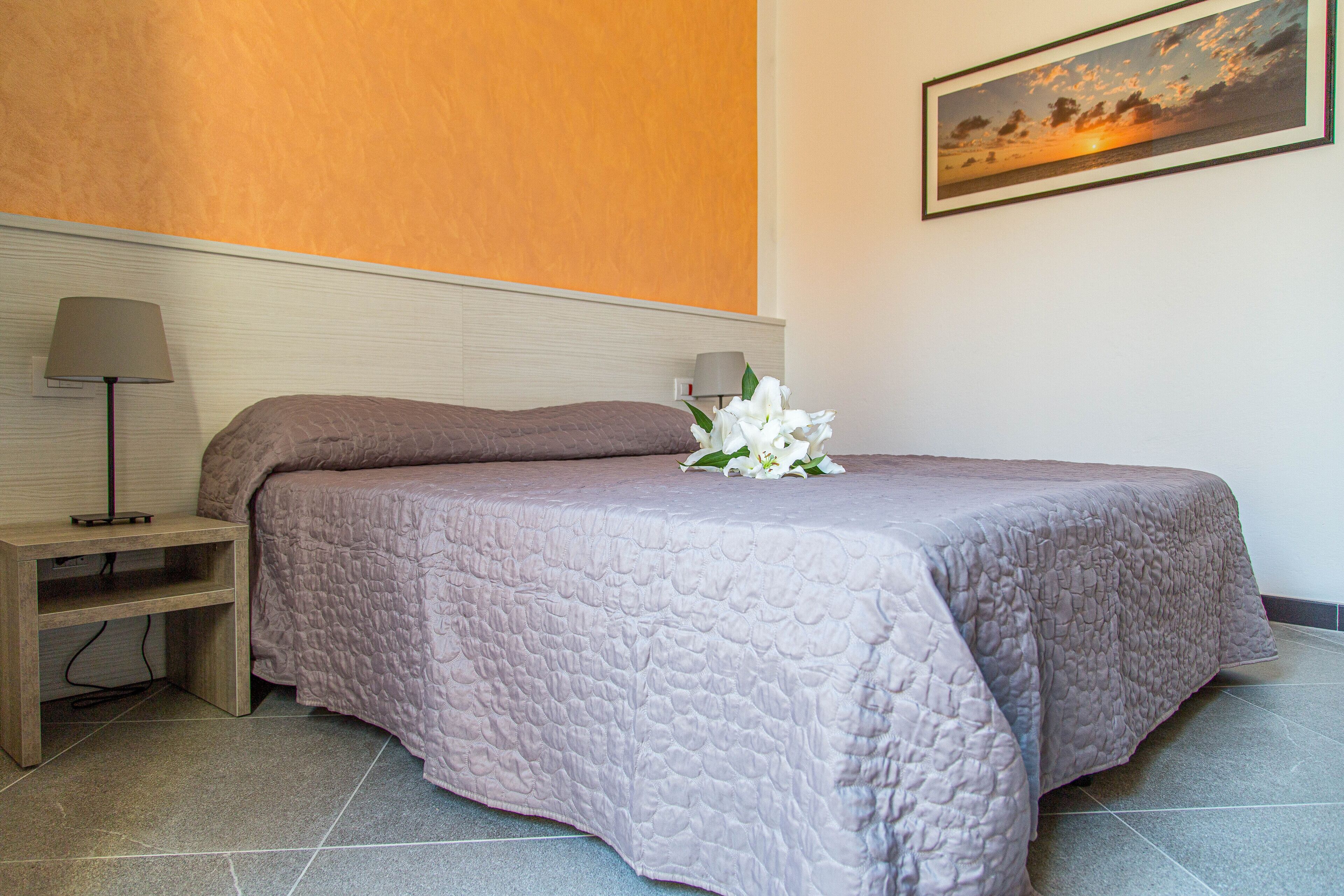 Un lit bien fait, recouvert d’une couverture à motifs, une table de chevet avec une lampe et un tableau encadré au mur.