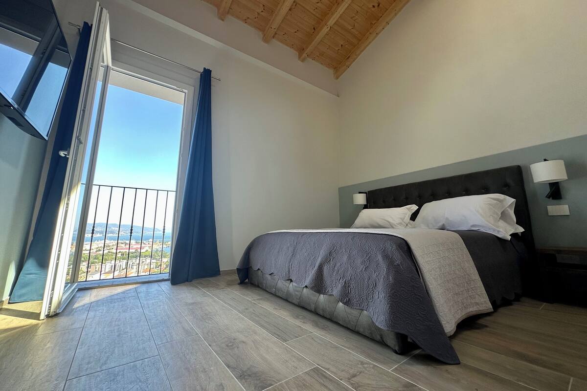Une chambre à coucher avec un lit, une table de chevet, une fenêtre avec des rideaux et une vue sur l’extérieur.