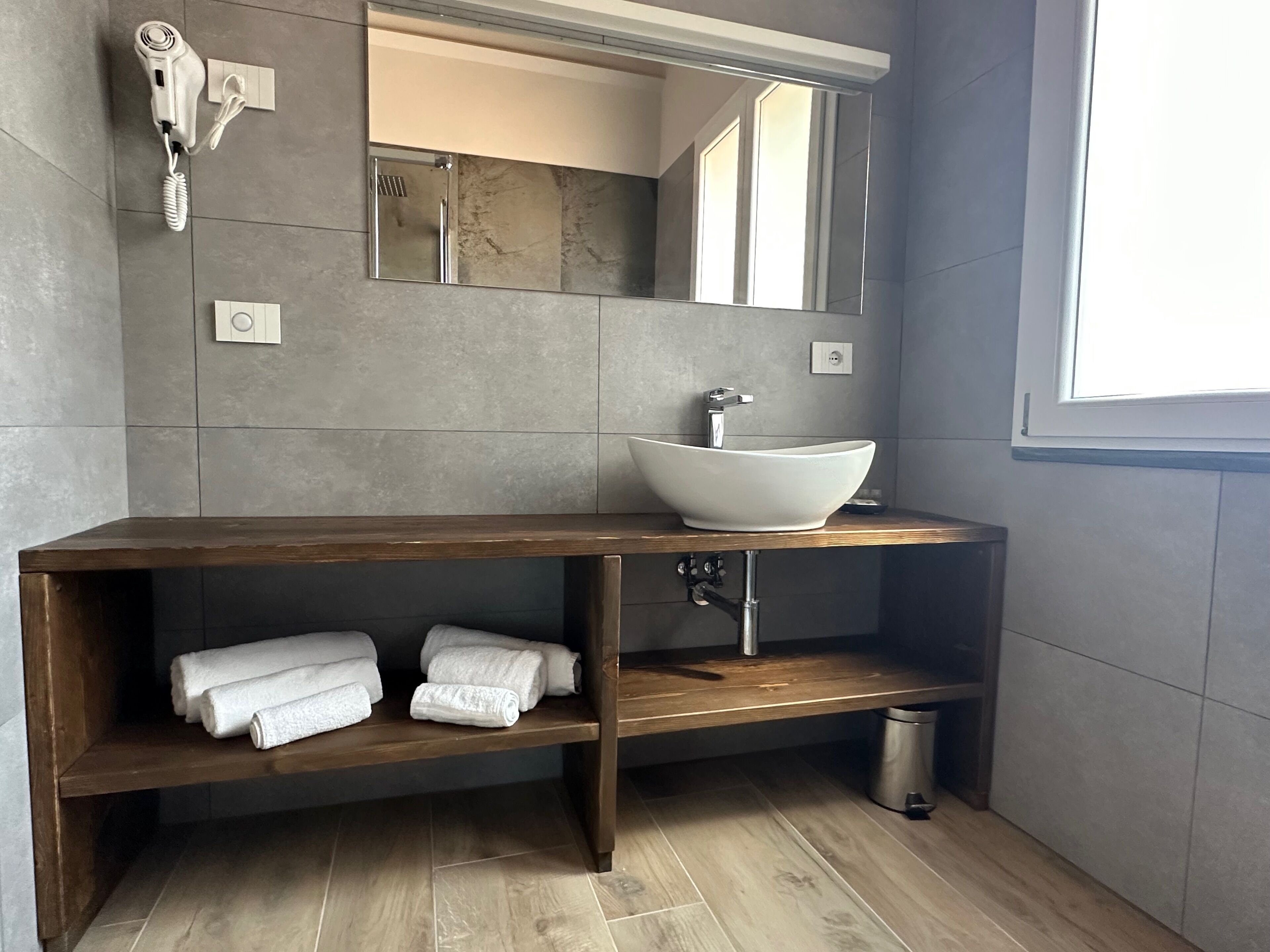 A modern bathroom with a wooden vanity, a white vessel sink, and a large mirror.