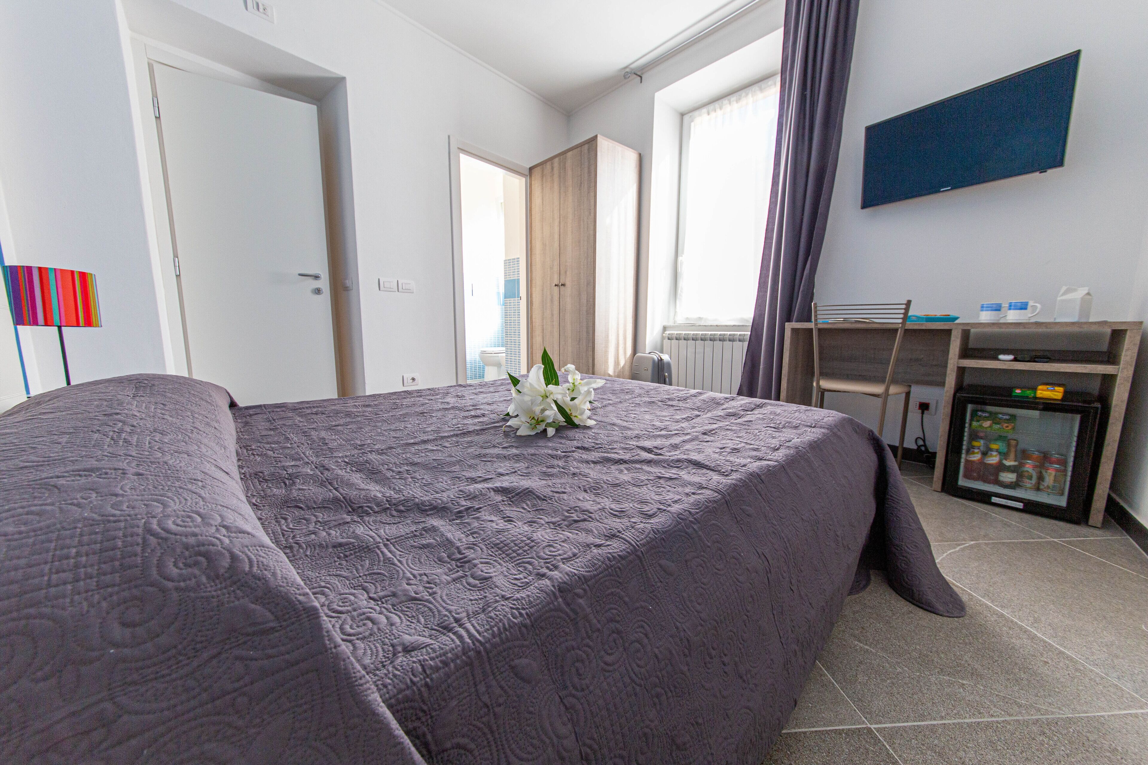 A hotel room with a bed, a desk, a refrigerator, and a window with curtains.
