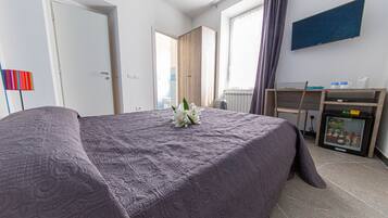 A hotel room with a bed, a desk, a refrigerator, and a window with curtains.