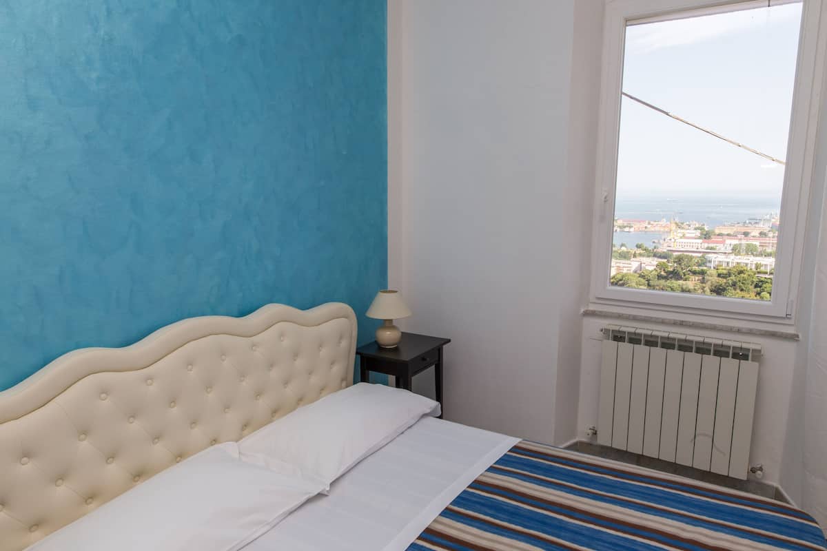 Une chambre à coucher avec un lit, une table de chevet, une fenêtre donnant sur la ville et un radiateur.