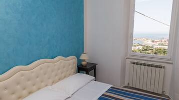 A bedroom with a bed, a nightstand, a window with a view of the city, and a radiator.