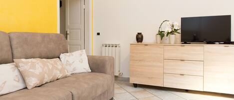 A living room with a beige sofa, a flat-screen TV, and a wooden cabinet.
