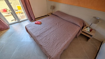 Un dormitorio con cama, mesita de noche, lámpara y vista al exterior.