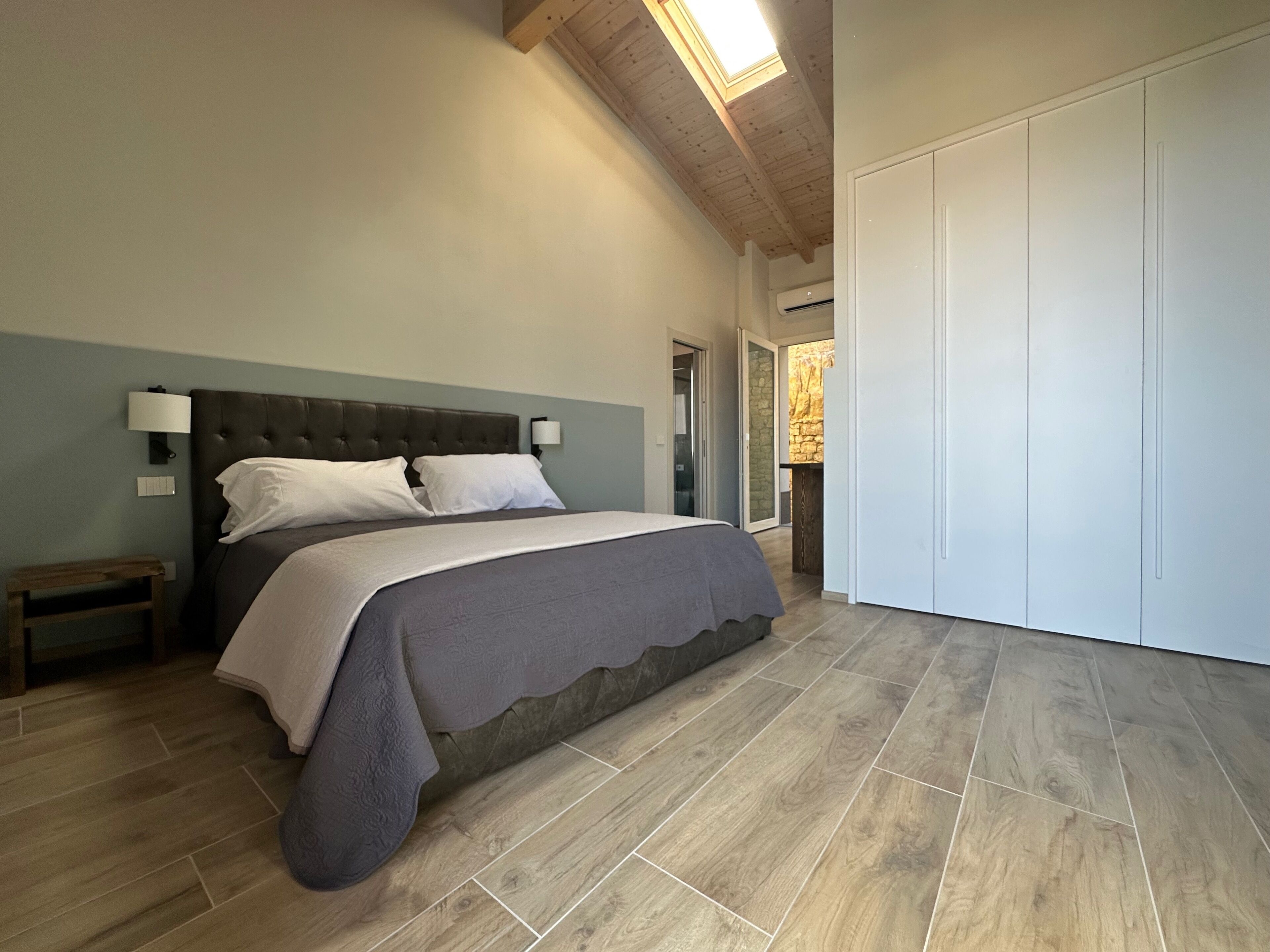 Een slaapkamer met een groot bed, houten vloeren, een plafond met zichtbare balken en een kledingkast.