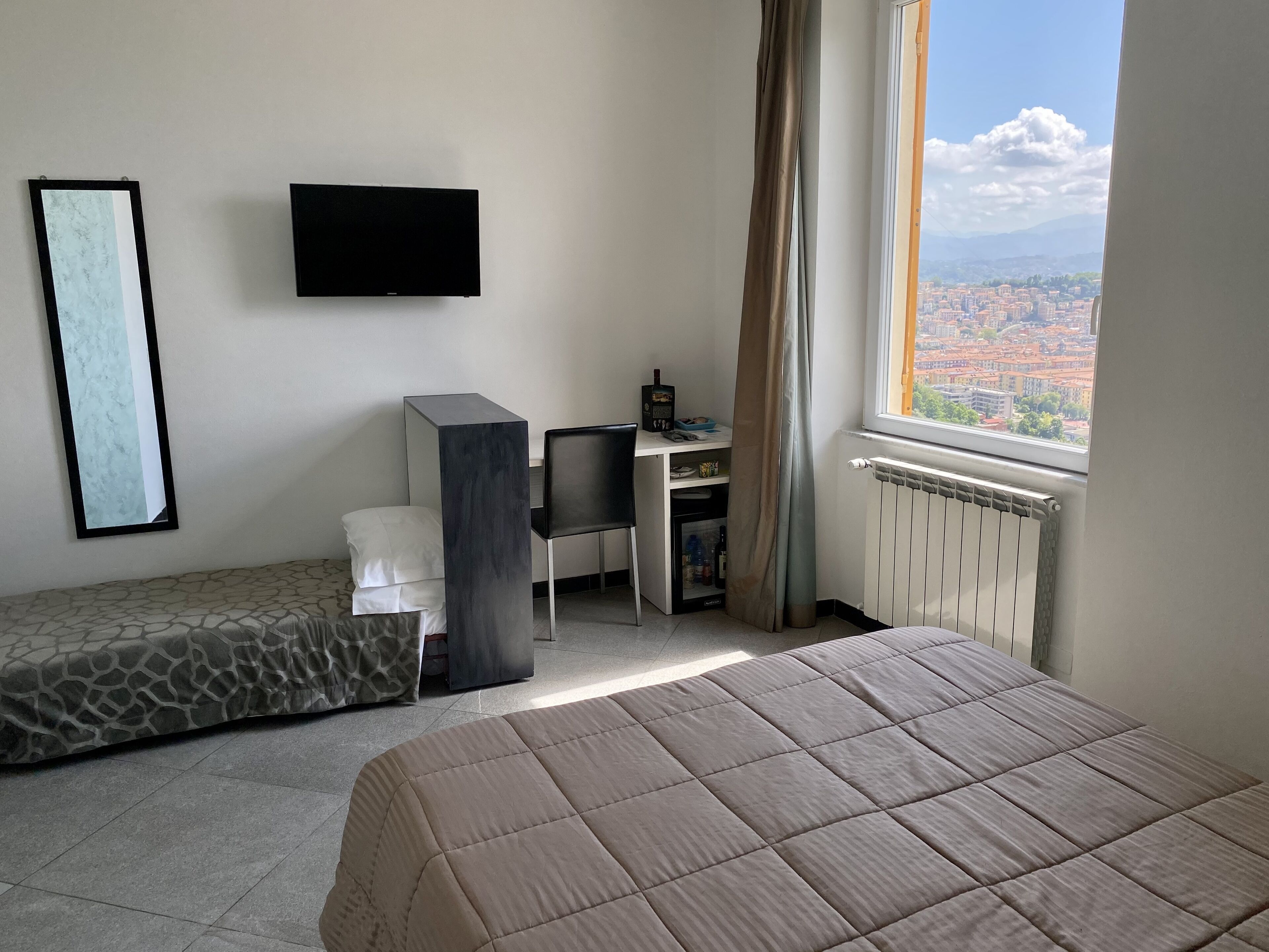 A bedroom with a bed, a desk, a chair, a TV, and a view of a cityscape.