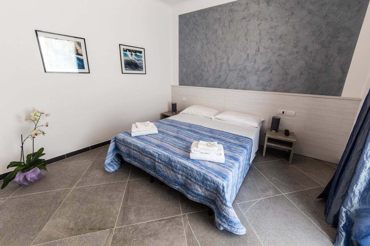 Une chambre d’hôtel moderne avec un grand lit, une table de chevet, un téléviseur fixé au mur et une plante en pot.