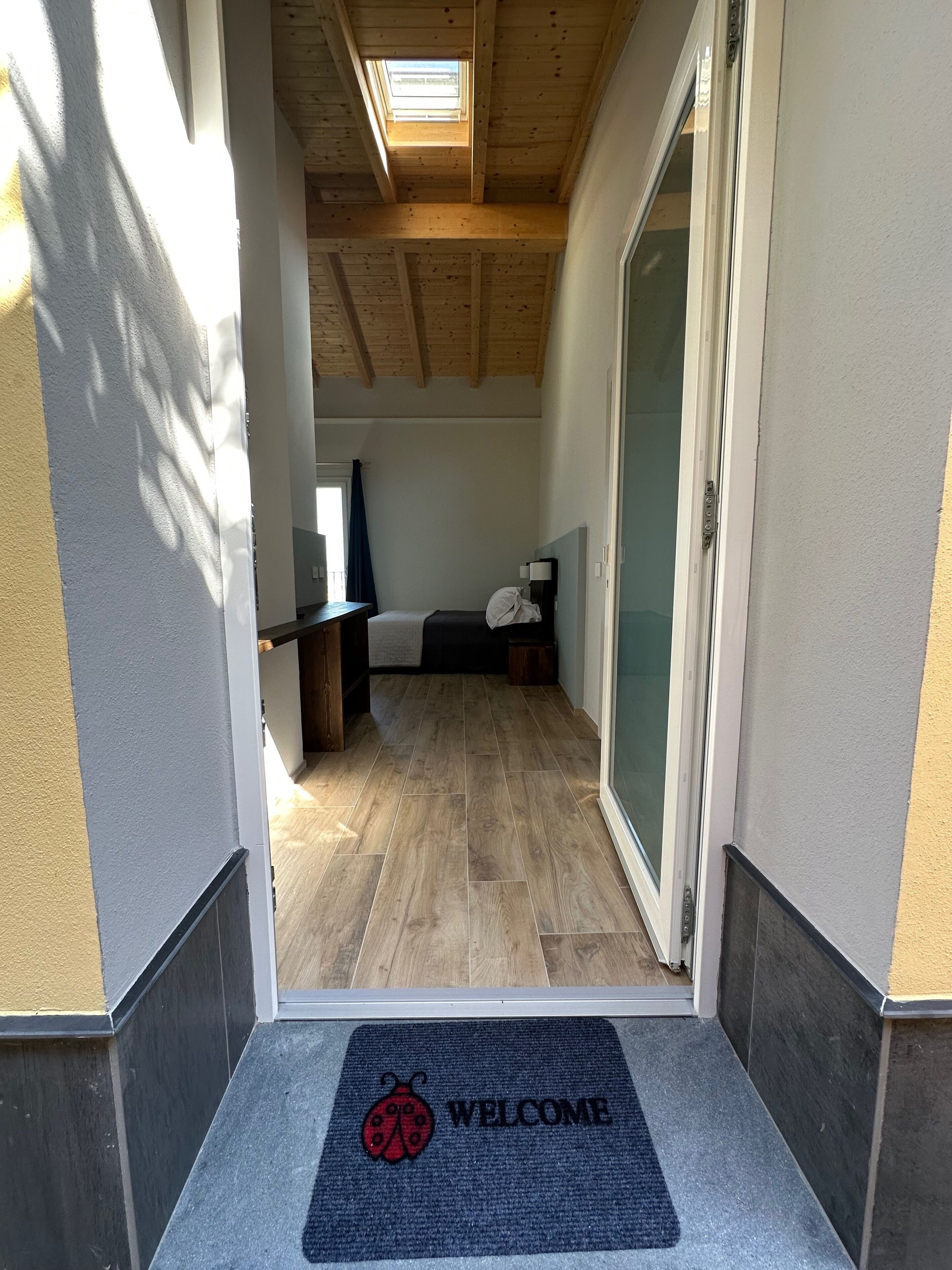Un pasillo estrecho con techo de madera, felpudo, cama y escritorio.