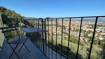 A balcony with a table and chairs, overlooking a cityscape with buildings and greenery.