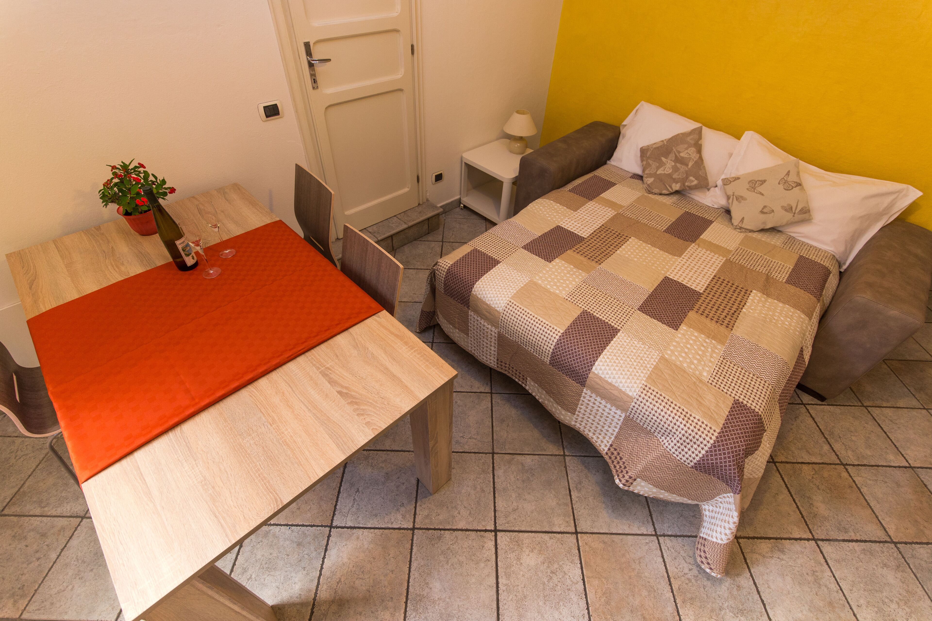 Ein Zimmer mit einem Bett, einem Tisch und einem Stuhl. Auf dem Tisch steht ein Blumentopf.