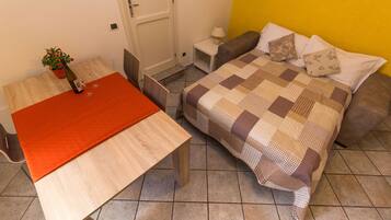 A room with a bed, a table, and a chair. There is a potted plant on the table.