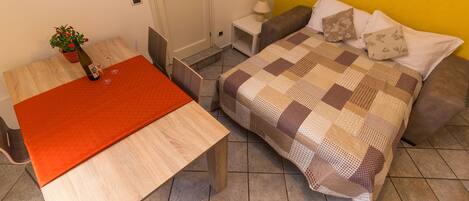 Ein Zimmer mit einem Bett, einem Tisch und einem Stuhl. Auf dem Tisch steht ein Blumentopf.