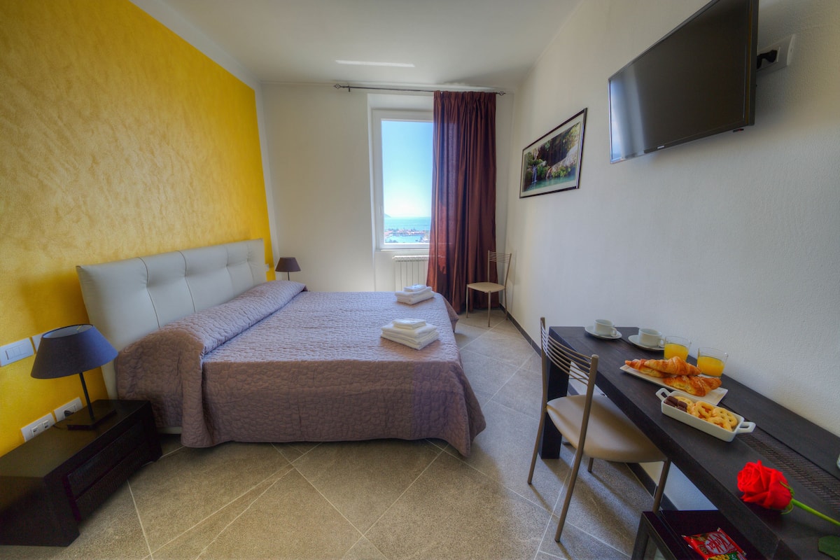 Une chambre d’hôtel avec un lit, un bureau avec un petit-déjeuner, une télévision et une fenêtre avec des rideaux.
