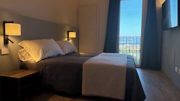 A bedroom with a bed, bedside lamps, a nightstand, a window with curtains, and a view of the outside.