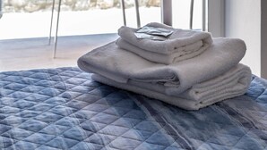A bed with a blue quilt, a chair, a table with a potted plant, and a stone wall in the background.