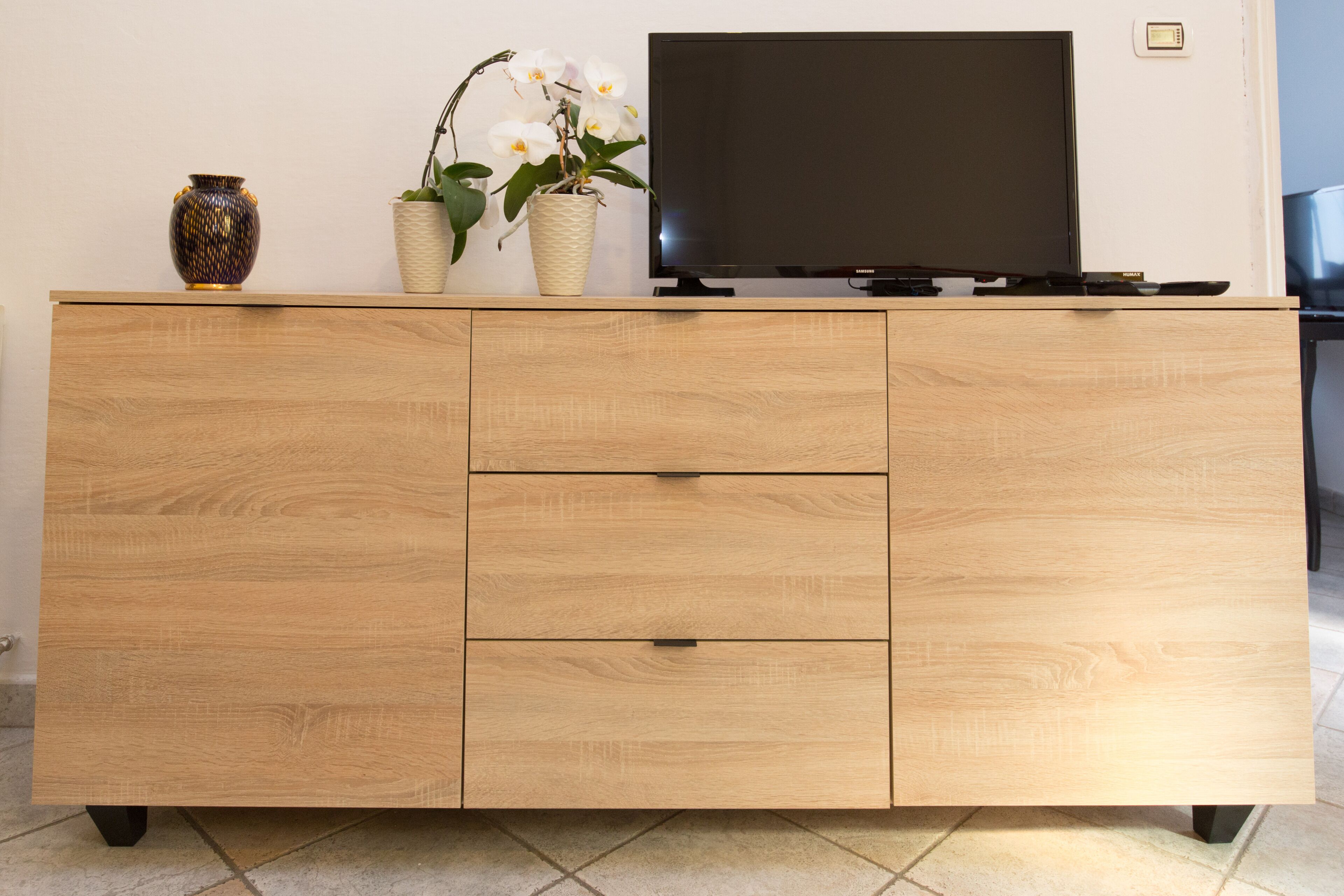 A wooden cabinet with a flat-screen TV on top, a vase, and a potted plant.