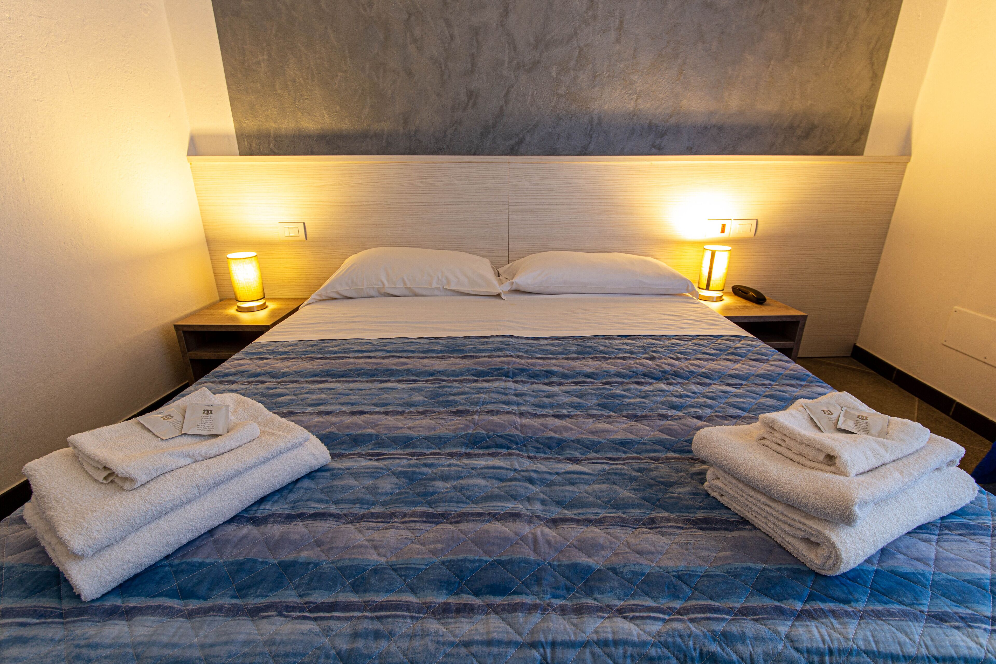 Un letto rifatto con una coperta blu, due lampade da comodino e asciugamani piegati su entrambi i lati.