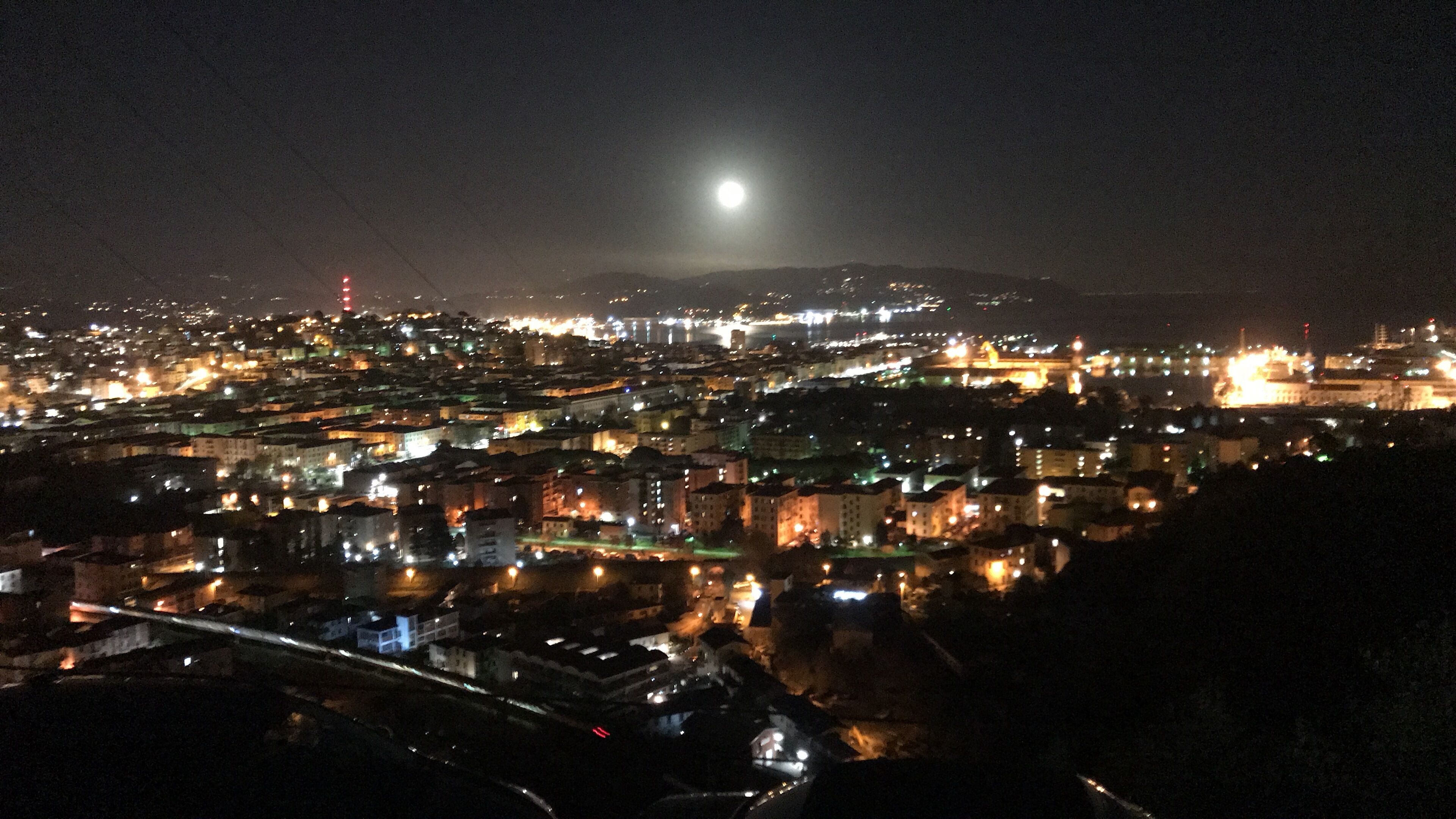 A nighttime cityscape with a prominent moon in the sky, illuminated buildings, and a distant castle-like structure.
