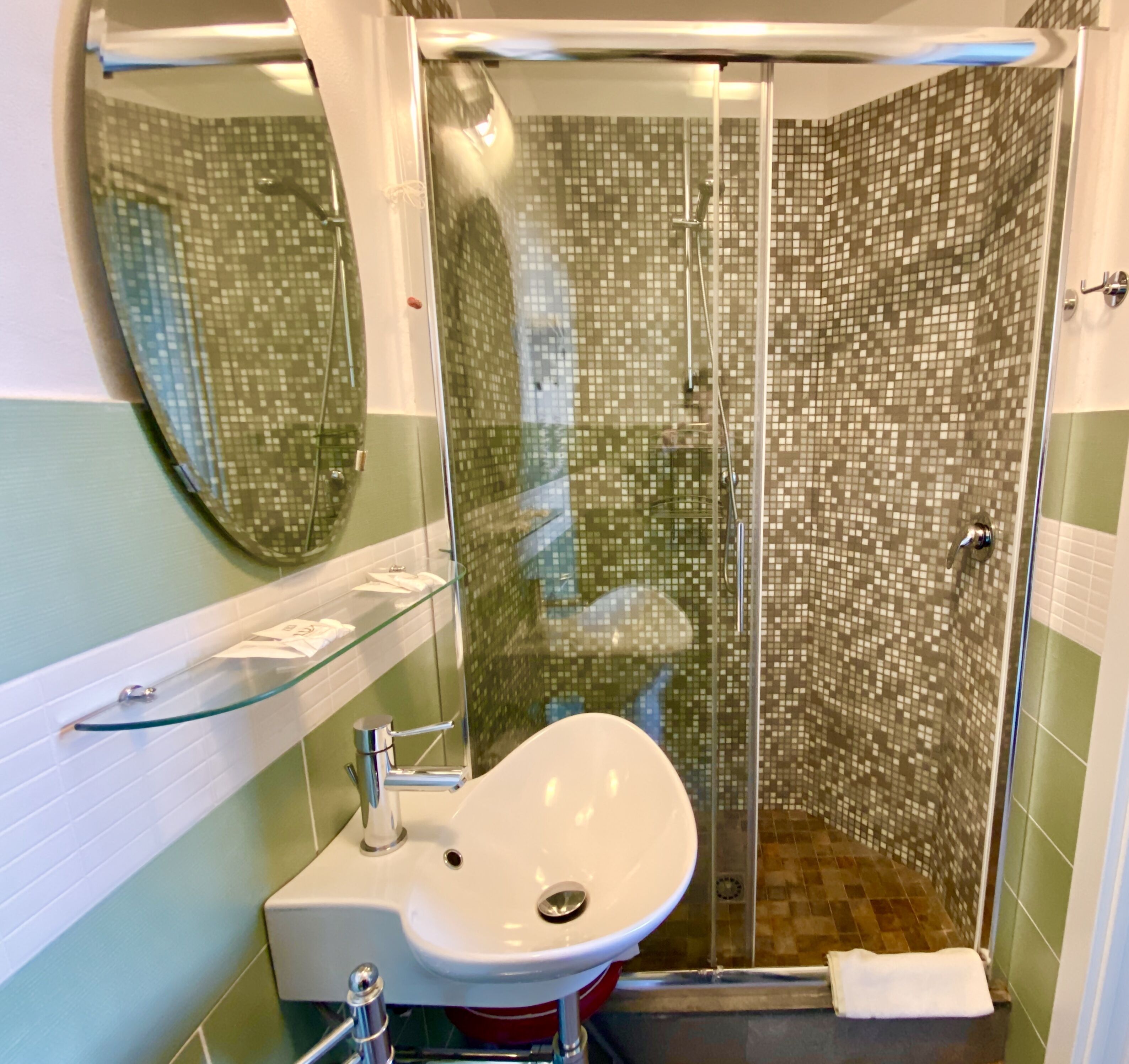 Un baño con ducha envuelta en vidrio, un lavamanos blanco y un espejo.
