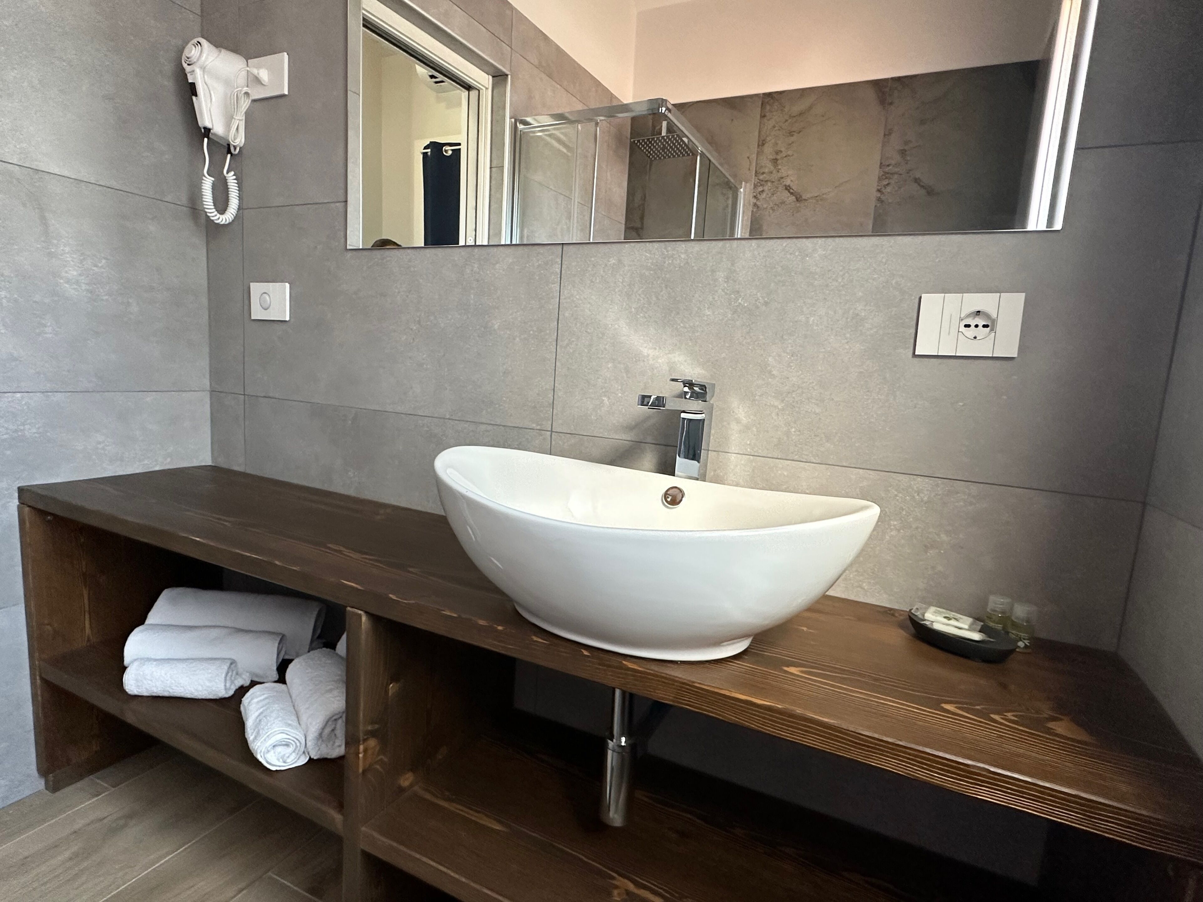 A bathroom with a large white sink, a wooden vanity, a towel rack, a hairdryer, and a mirror.