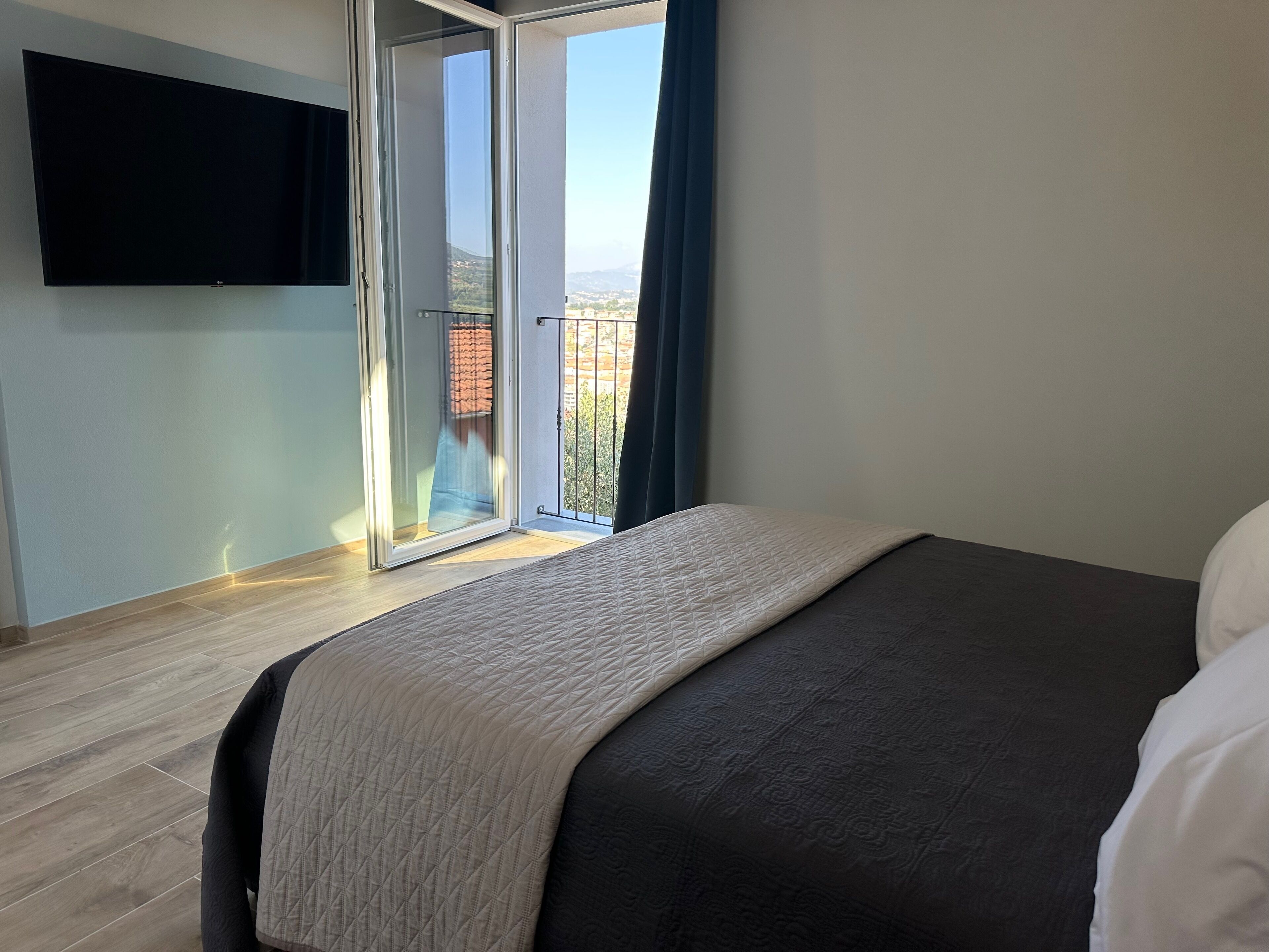 Una camera da letto con un letto, una TV montata a parete e una porta scorrevole in vetro che dà su un balcone.