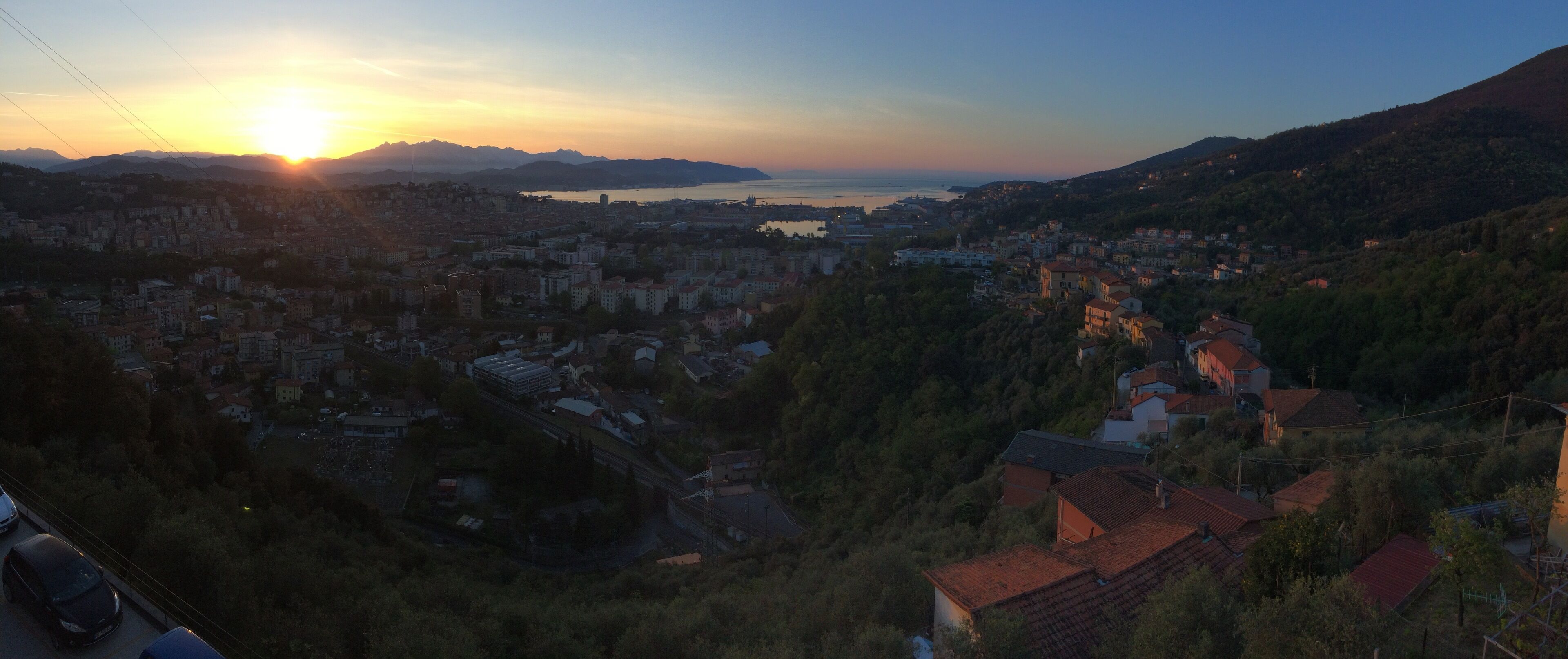 A panoramic view of a coastal city during sunset with buildings, a bridge, and a body of water.