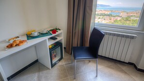 A breakfast setup with croissants, a red rose, and a view of a coastal city through a window.
