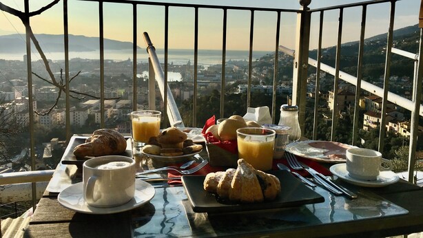 A breakfast table with croissants, juice, and coffee, overlooking a cityscape.