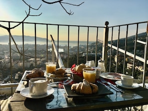 Una mesa de desayuno con cruasanes, jugo y café, con vistas a un paisaje urbano.