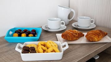 A breakfast setting with pastries, a blue container of chocolates, and two white cups on a wooden table.