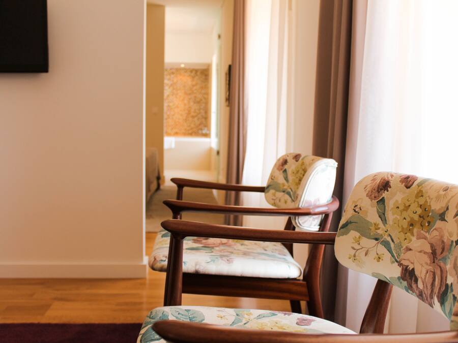 Una habitación con una silla de madera tapizada con motivos florales, suelo de madera y un televisor montado en la pared.