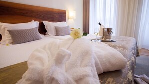 A hotel room with a large bed, a wooden headboard, a bedside table with a wine glass and a silver pitcher, and a white rose on the bed. - Convento da Serta Hotel (Serta)