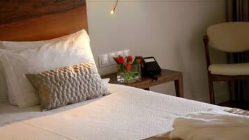 A neatly made bed with white linens, a wooden headboard, and a bedside table with a vase of red roses and a telephone.
