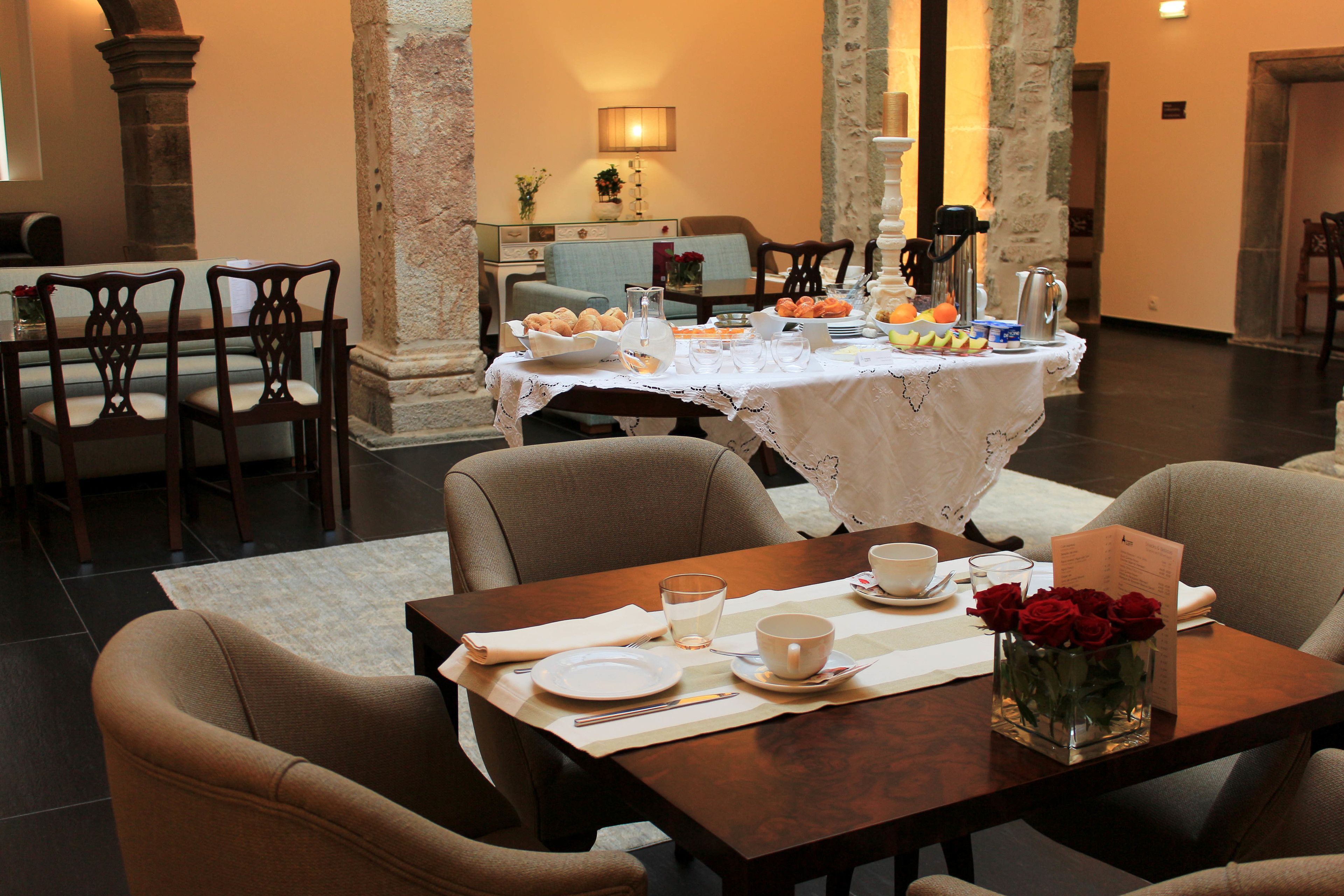 Un comedor con una mesa dispuesta para dos, un jarrón de rosas rojas y una mesa de buffet al fondo.