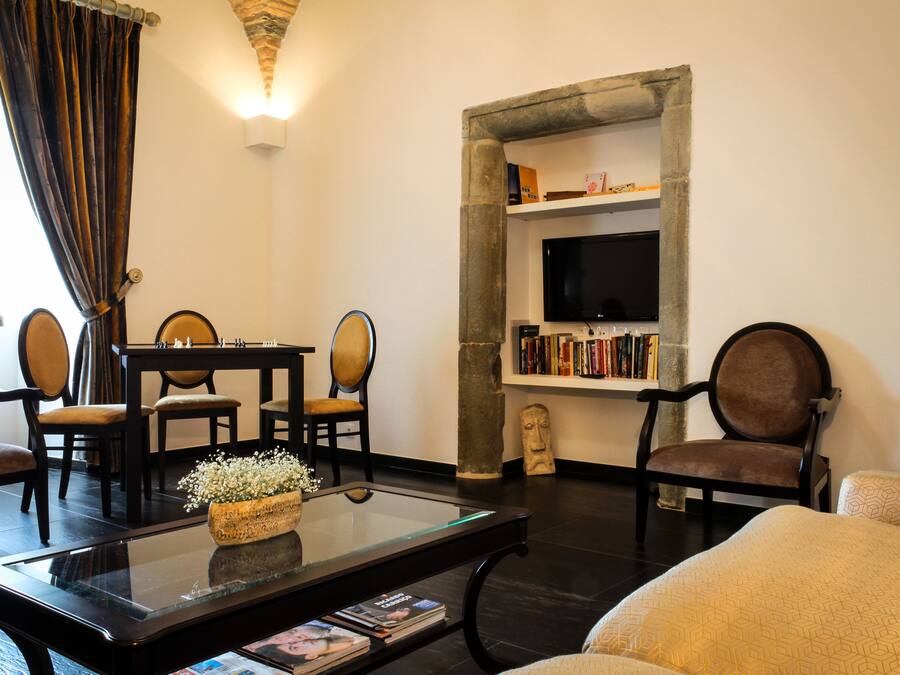 A living room with a glass coffee table, a sofa, a television, and a stone wall with bookshelves.