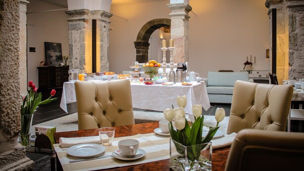 A dining area with a table set for two, featuring a vase of white tulips, a fruit bowl, and a coffee pot. - Convento da Serta Hotel (Serta)