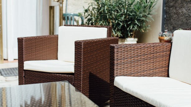 Wicker furniture with white cushions, a glass table, and a potted plant in the background.