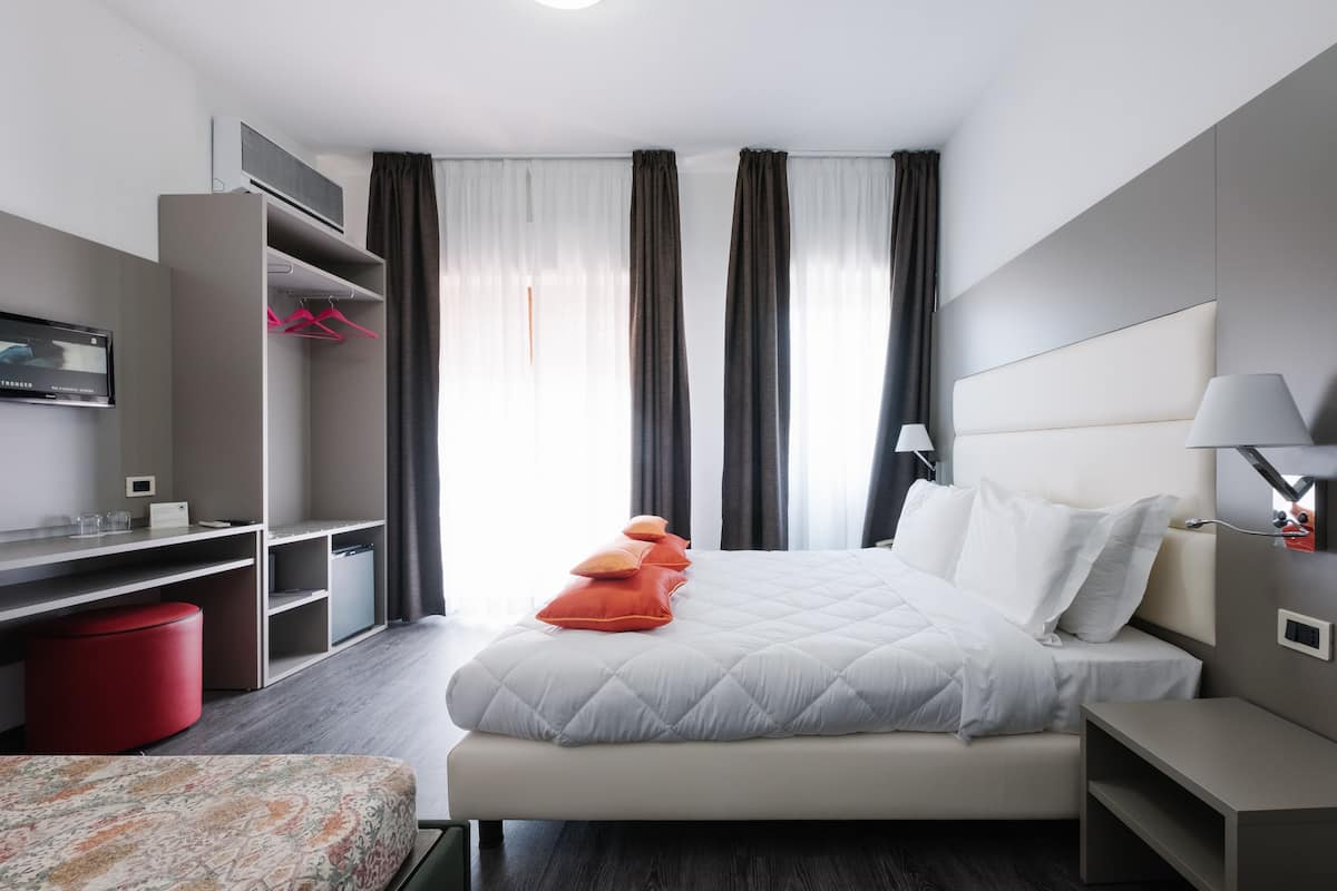 A modern hotel room with a bed, a desk, a TV, and a wardrobe.