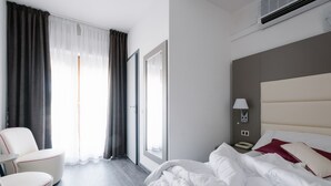 A hotel room with a bed, a chair, a nightstand, a lamp, and a window with curtains.
