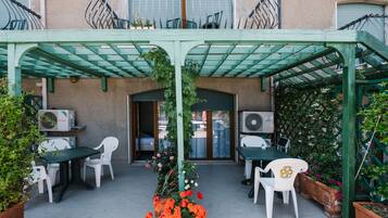 Patio esterno con tavoli e sedie, circondato da vasi con piante e fiori.