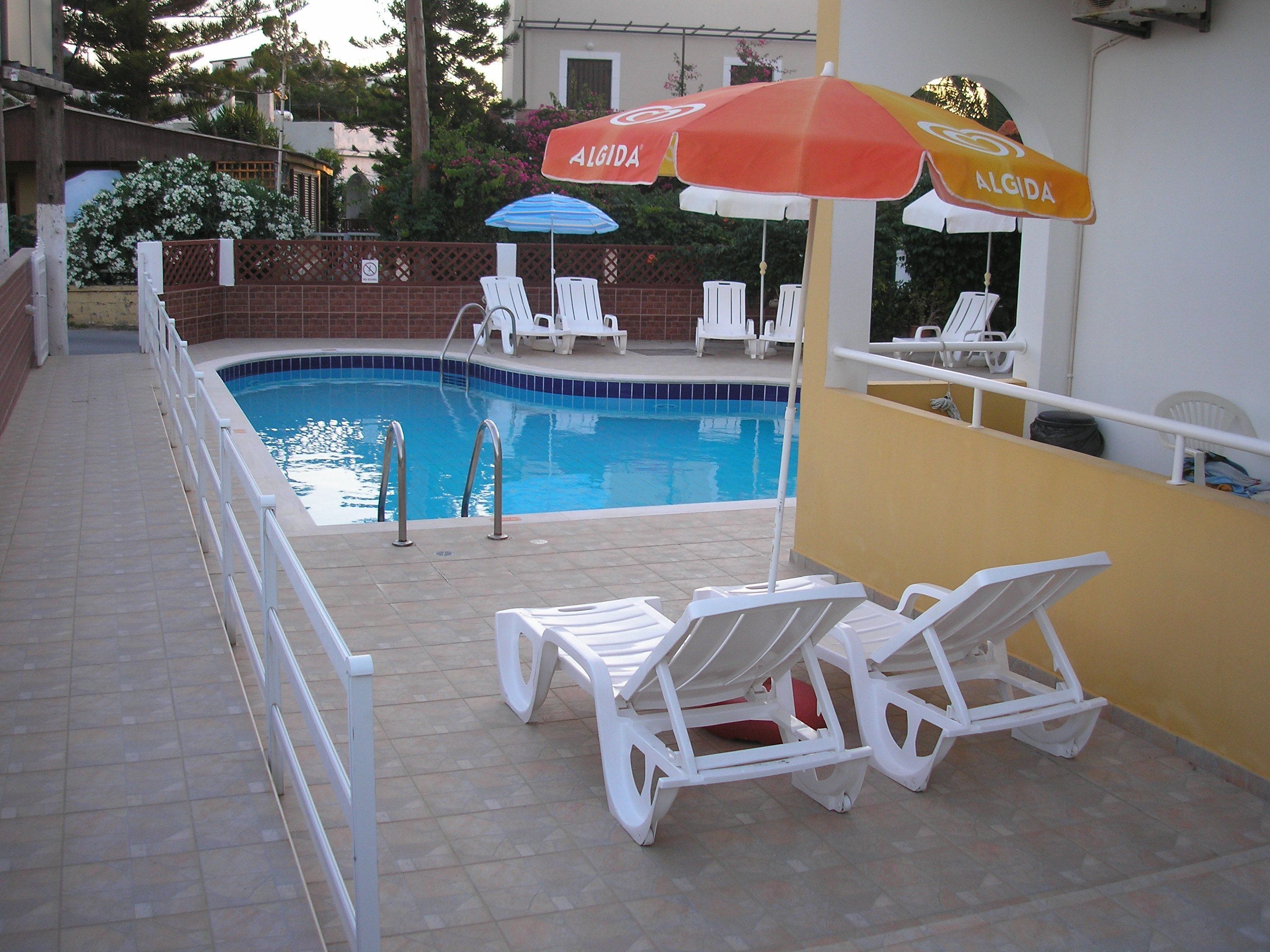 A swimming pool with white lounge chairs and two umbrellas labeled 'ALGIDA'.