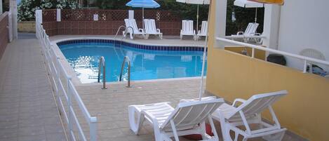A swimming pool with white lounge chairs and two umbrellas labeled 'ALGIDA'.