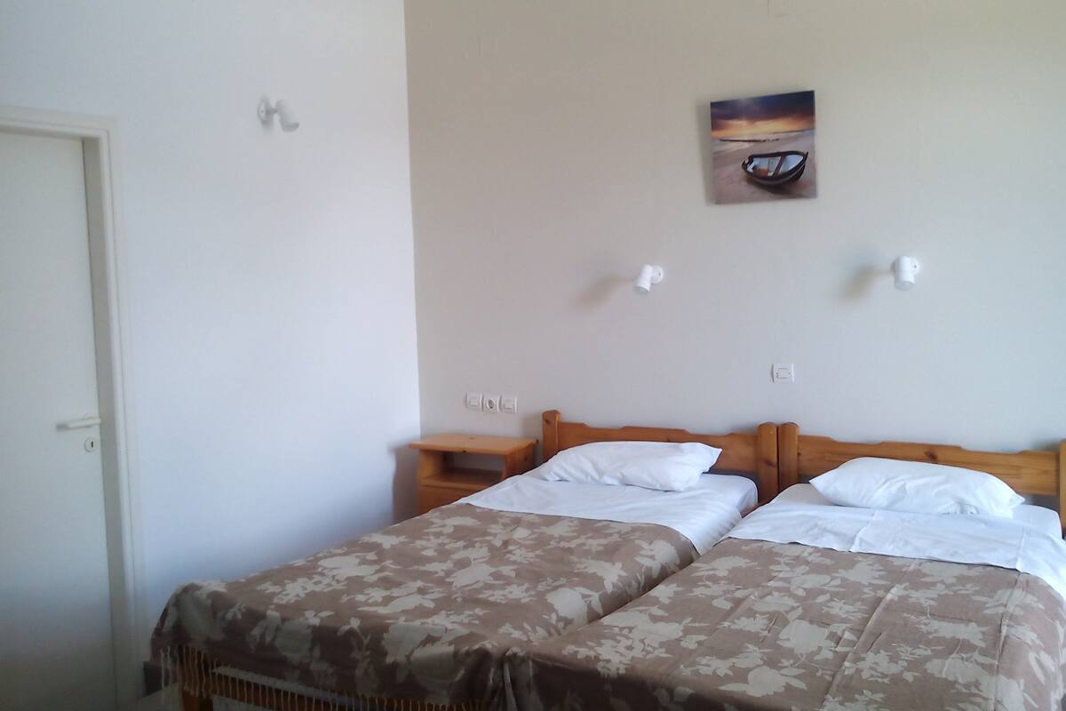 A bedroom with two beds, a wooden headboard, a nightstand, and a wall-mounted light fixture.